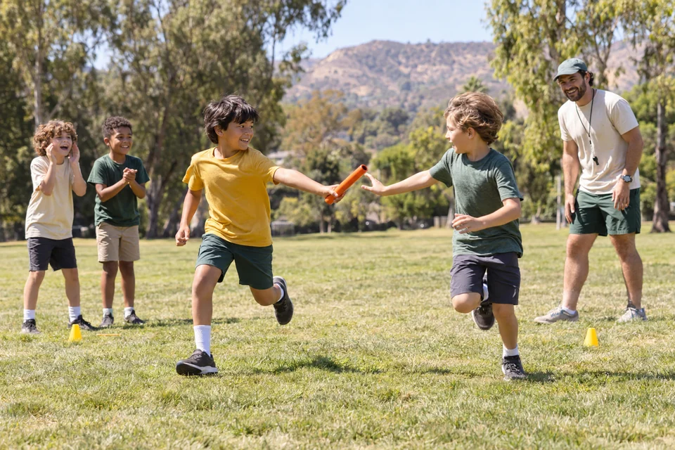 Campers passing a relay baton and cheering teammates on a sunny field
